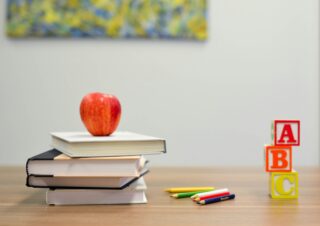 A charter school table with a stack of books and an apple, colored pencils, and ABC blocks