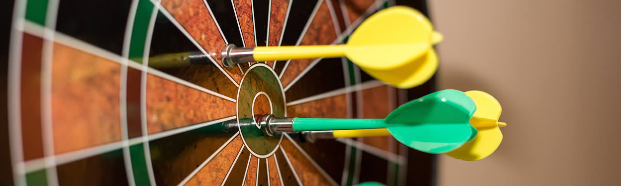 A red and black dart board with yellow darts near the bullseye and a green dart in the bullseye